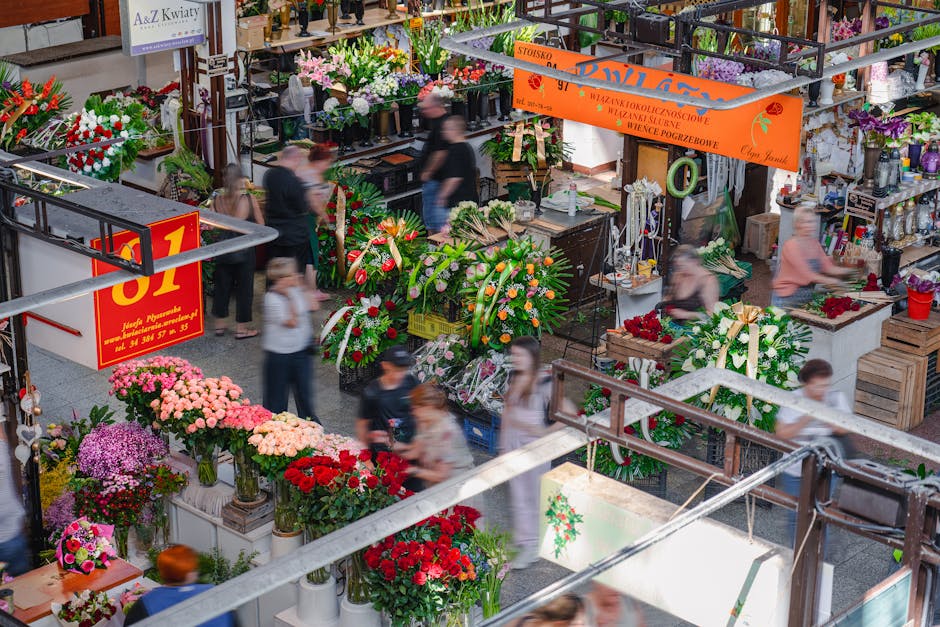 An indoor flower market scene at East Finchley Florist, showcasing an array of fresh floral arrangements and bouquets. Prominent in the foreground are vibrant red and pink roses, along with purple and